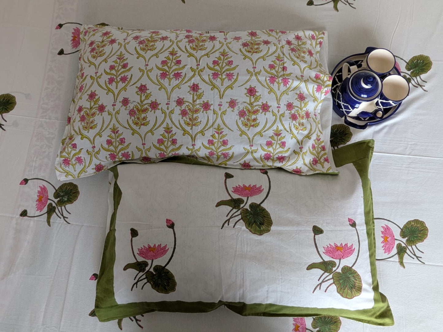 Two decorative reversible pillows with floral patterns on a white bedsheet background.