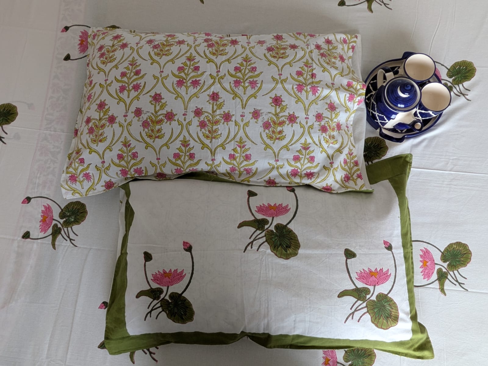 Two decorative reversible pillows with floral patterns on a white bedsheet background.