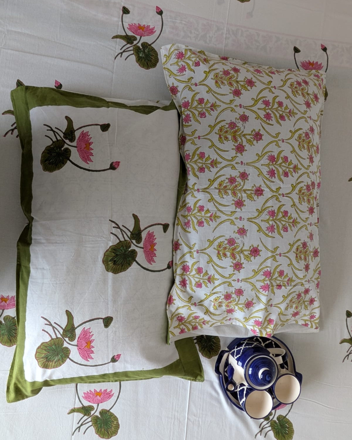 Two decorative reversible pillows with floral patterns on a white bedsheet background.