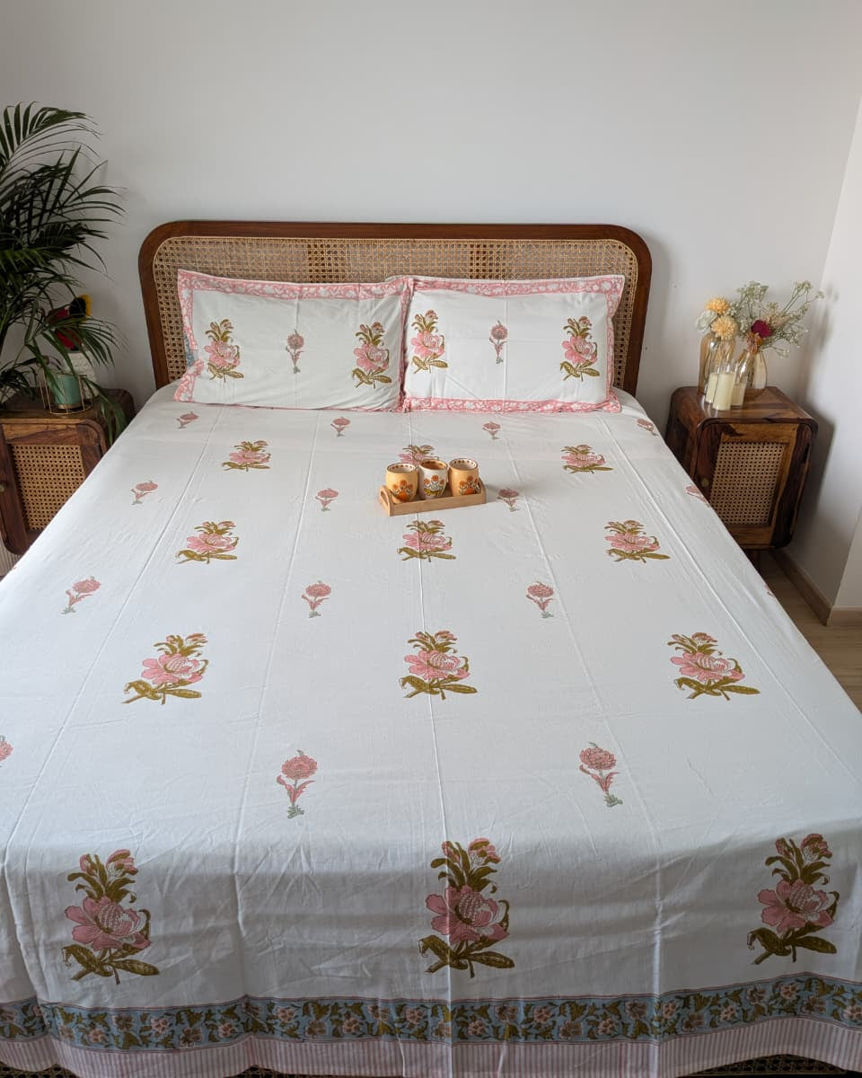 Bed with cotton floral patterned bedsheet and matching reversible pillows in a bedroom setting.