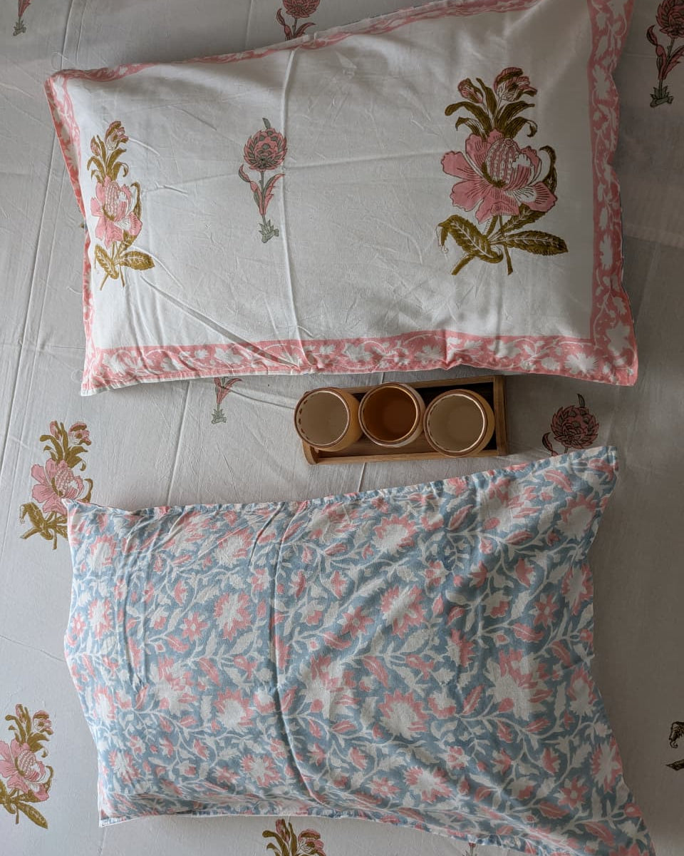 Two reversible cotton floral-patterned pillows on a bed with a decorative headboard.
