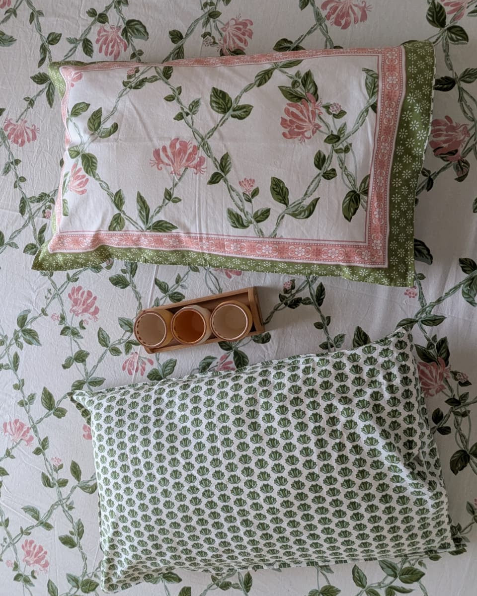 Two patterned pillows on a floral bedsheet with a small wooden tray and cups.