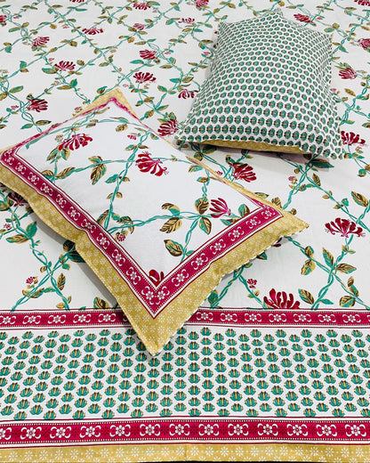 Close-up of red floral cotton bedsheet with a crimson bordered pillow cover and green dotted cushion