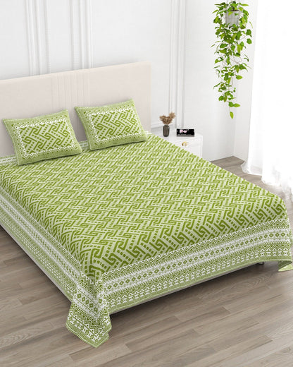 Leher Green bedsheet, leaf-green interlocking key-pattern print, in a studio shot against a cream headboard