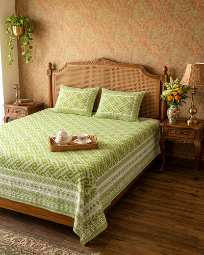 Leher Green bedsheet, leaf-green interlocking key-pattern print, on a bed with a cane headboard and a tea tray