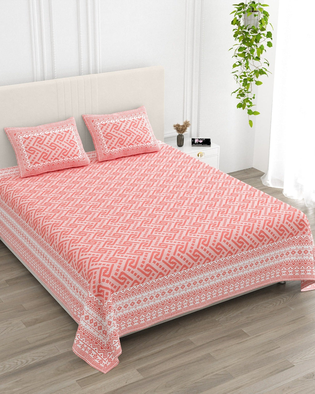 Leher Pink bedsheet, coral-pink interlocking key-pattern print, in a studio shot against a cream headboard