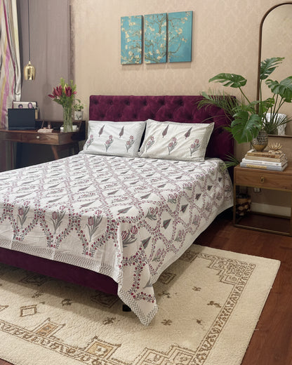 Bed with floral patterned bedspread and pillows in a room setting.