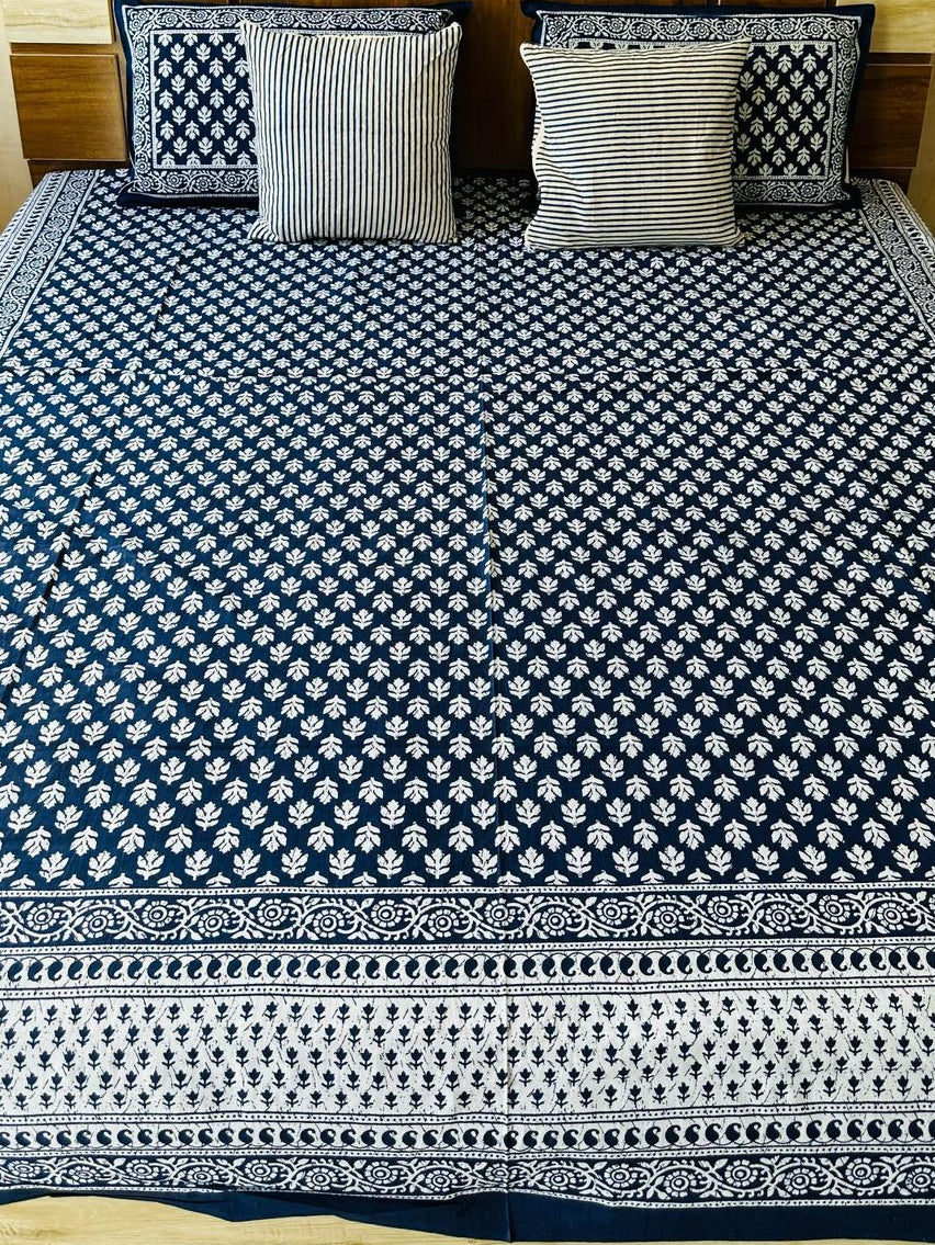 Bed with blue and white patterned bedspread and pillows against a beige wall.