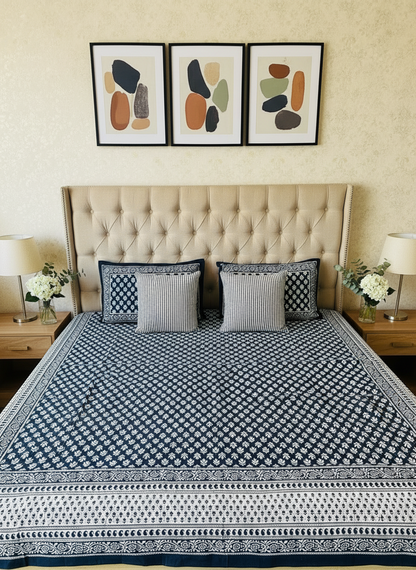 Bed with blue and white patterned bedspread and pillows against a beige wall.