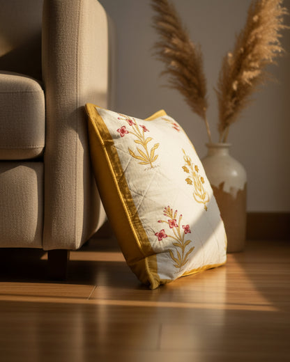 Mehek yellow quilted cushion cover styled beside a chair, showing pink and ochre flowers