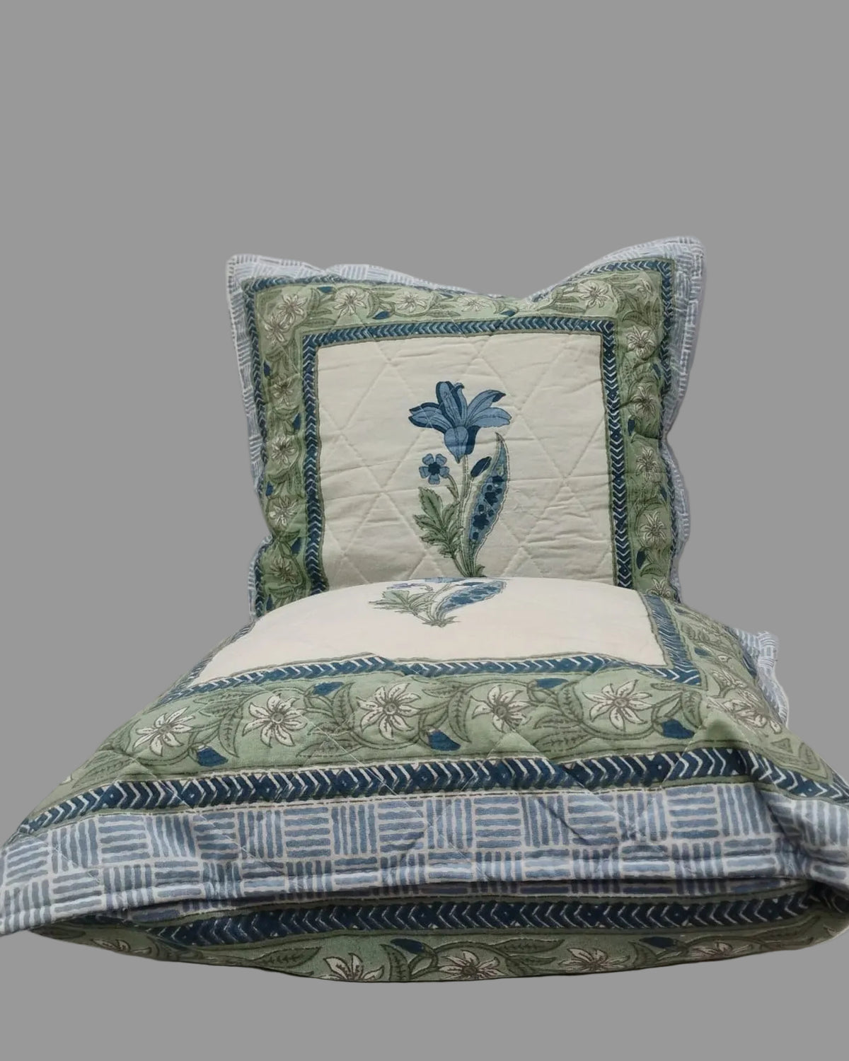 Two Mridula blue quilted cushion covers stacked to show the floral borders and striped reverse