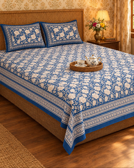 Padmaja Blue bedsheet with ivory florals on navy and a striped border, with a tea tray on a cane-headboard bed