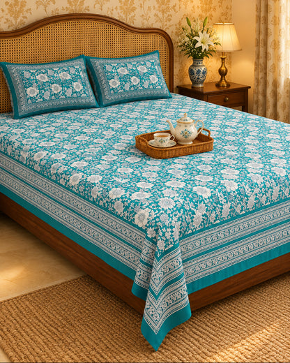Padmaja Teal bedsheet with ivory florals and a striped border, with a tea tray on a cane-headboard bed