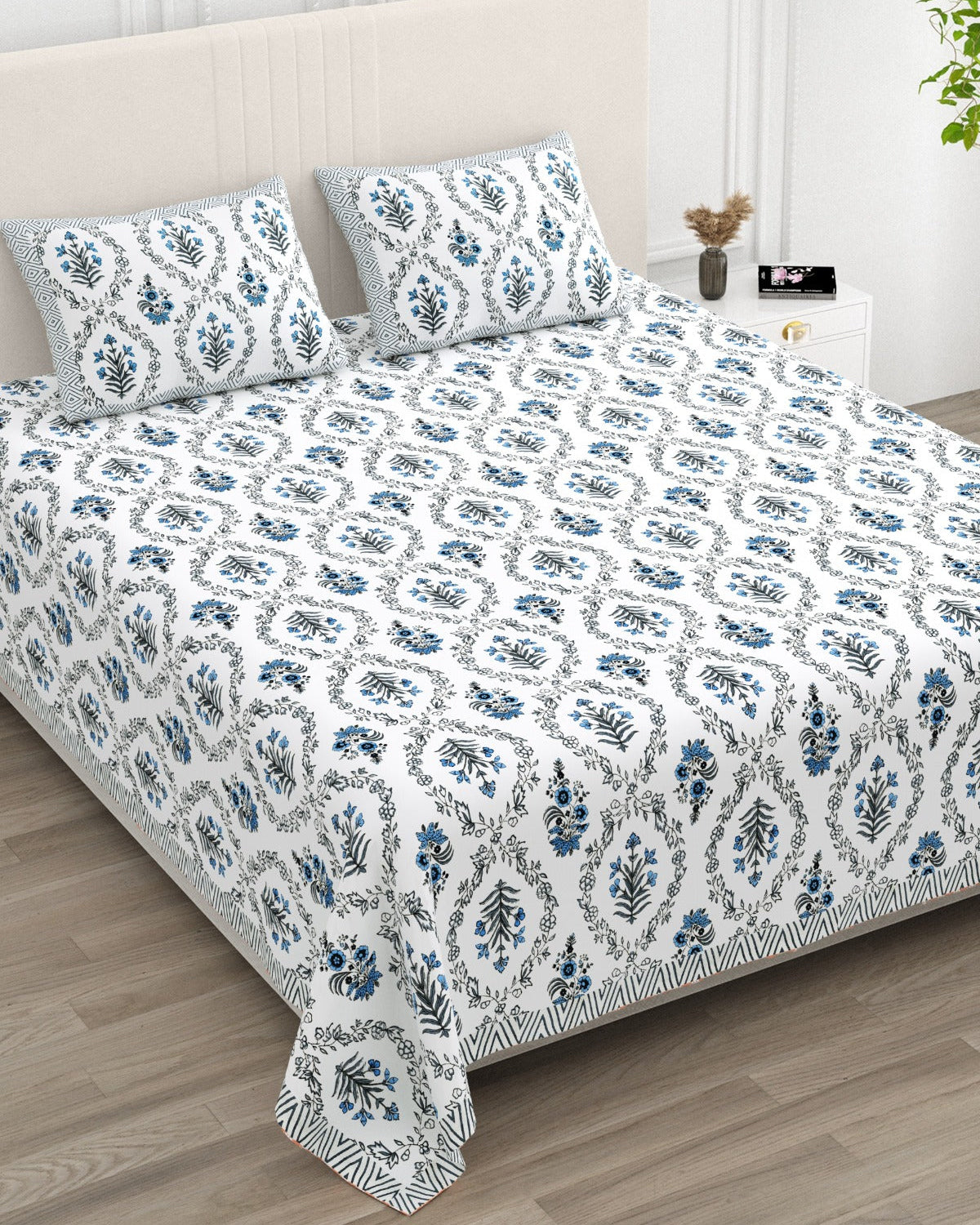 Parijat Blue bedsheet, white floral ogee jaal with blue flowers, in a studio shot against a cream headboard