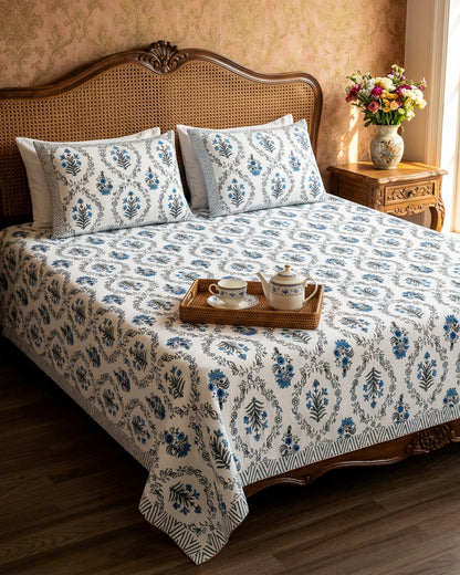 Parijat Blue bedsheet, white floral ogee jaal with blue flowers, on a bed with a cane headboard and a tea tray