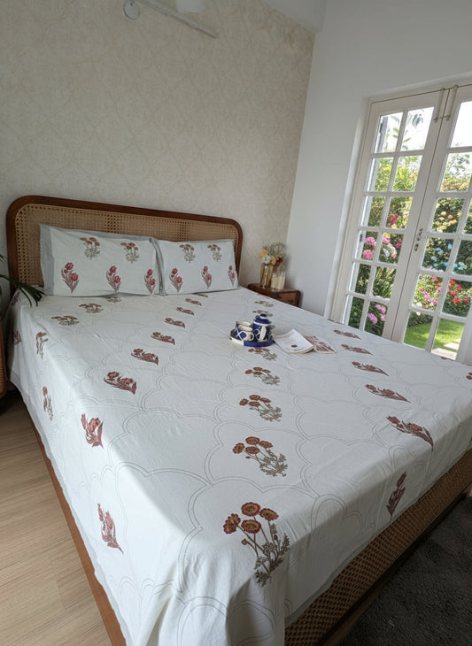 Bed with floral bedding in a room with a white wall and wooden floor.