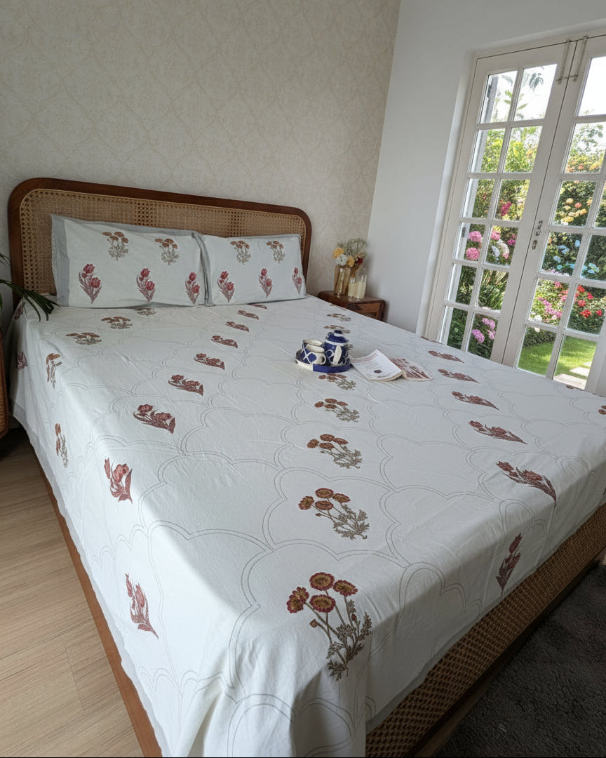 Bed with floral bedding in a room with a white wall and wooden floor.