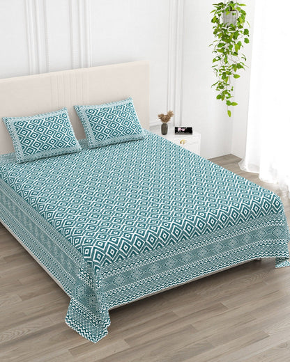 Ratna Blue bedsheet, all-over teal nested-diamond print, in a studio shot against a cream headboard