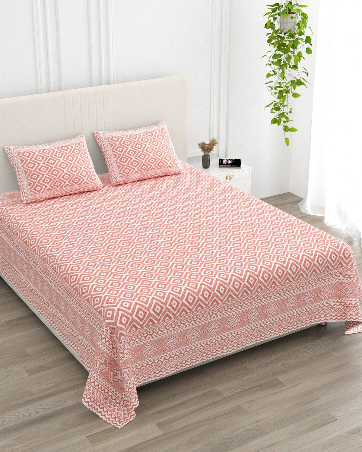 Ratna Pink bedsheet, all-over coral-pink nested-diamond print, in a studio shot against a cream headboard