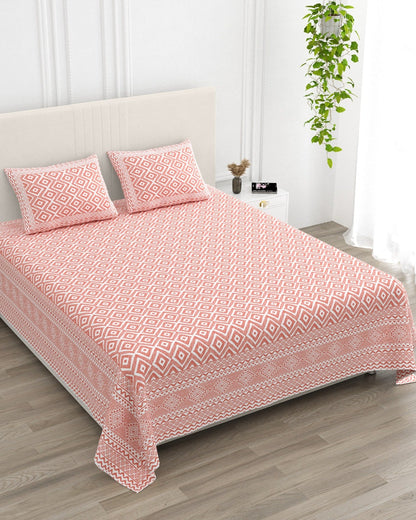 Ratna Pink bedsheet, all-over coral-pink nested-diamond print, in a studio shot against a cream headboard