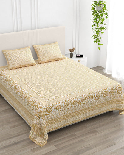 Sagar Beige bedsheet, mustard-gold geometric maze with a medallion-flower border, in a studio shot against a cream headboard