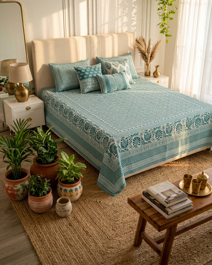 Sagar Blue bedsheet, teal geometric maze with a medallion-flower border, on a bed with a cream headboard with potted plants and a jute rug