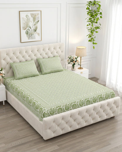Sagar Green bedsheet, sage-green geometric maze with a medallion-flower border, on a tufted ivory bed