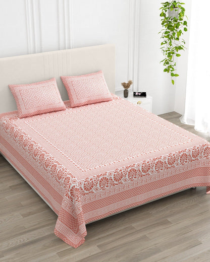 Sagar Pink bedsheet, coral-pink geometric maze with a medallion-flower border, in a studio shot against a cream headboard