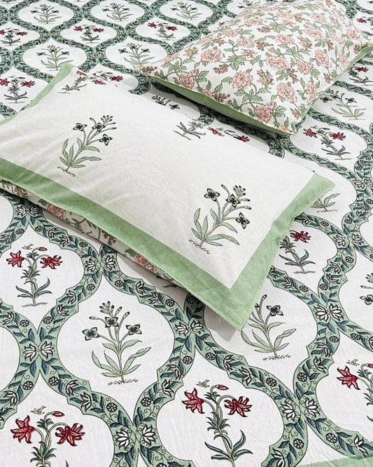 Bed with floral-patterned bedsheet and 2 reversible pillows in green and red