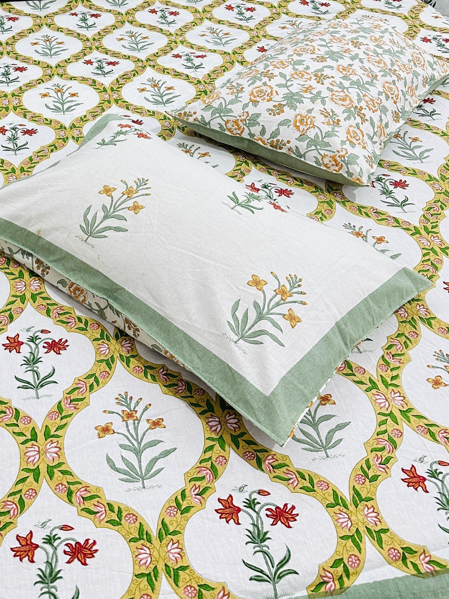 Bed with floral patterned bedsheet and 2 reversible pillow in green yellow and red
