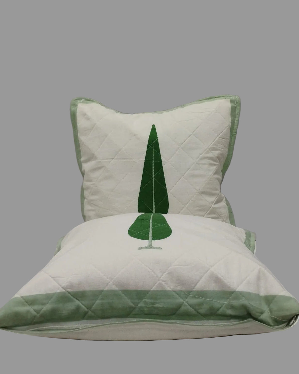 Two Suparna green quilted cushion covers stacked to show the tree motif and green trim