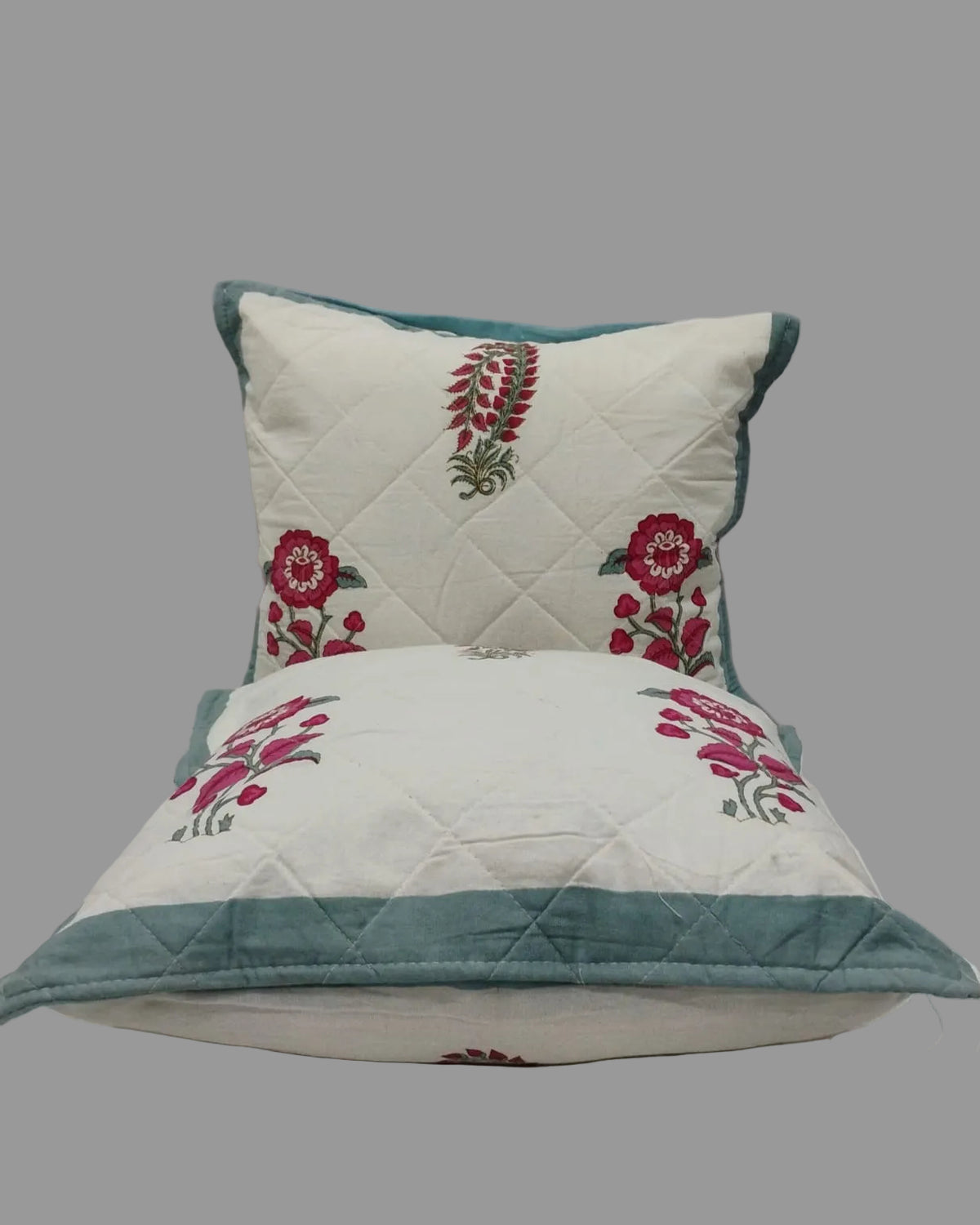 Two Surmayi blue quilted cushion covers stacked to show the floral print and teal trim