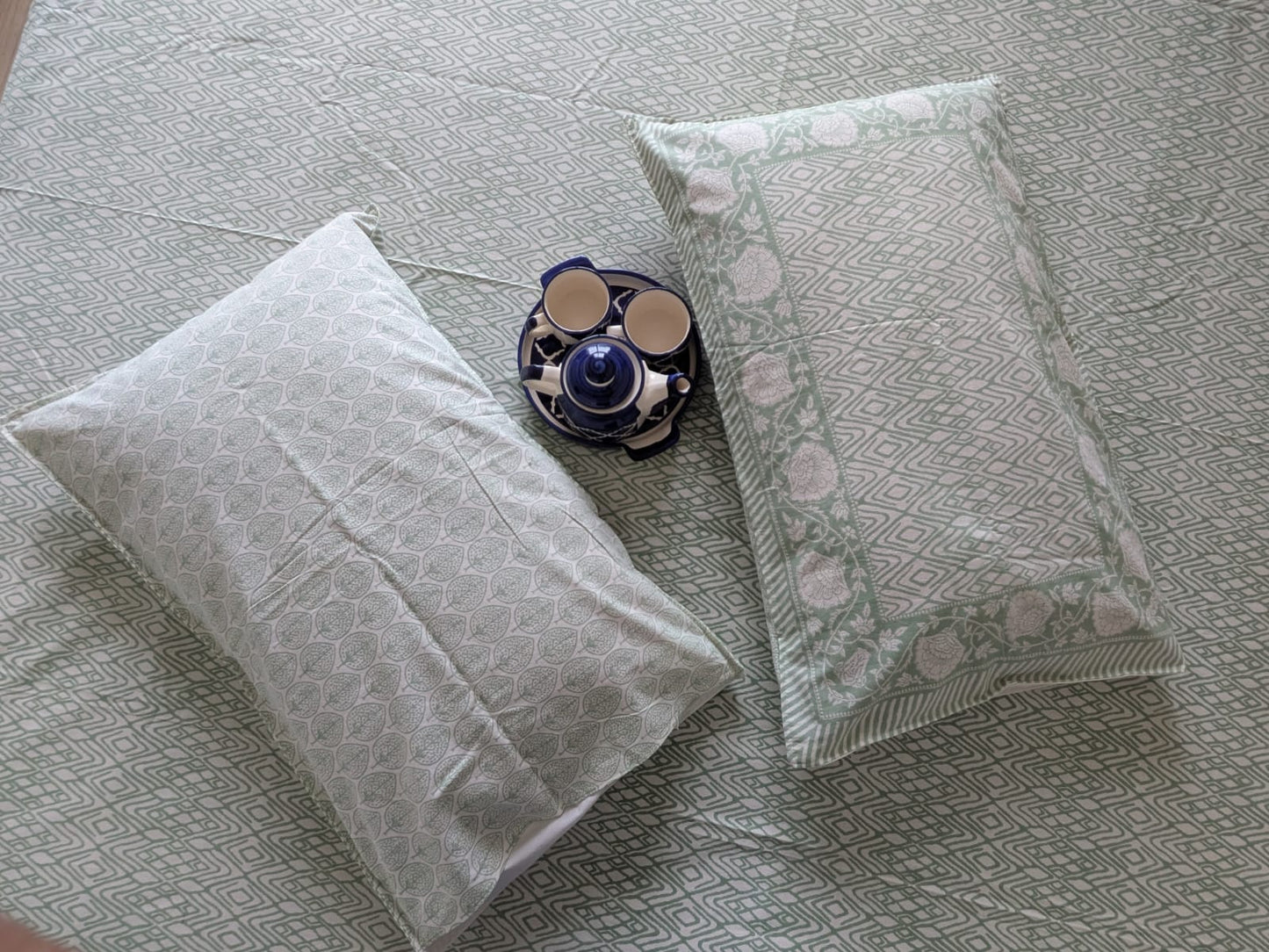 Two patterned pillows on a textured bedsheet with a decorative item in the center.