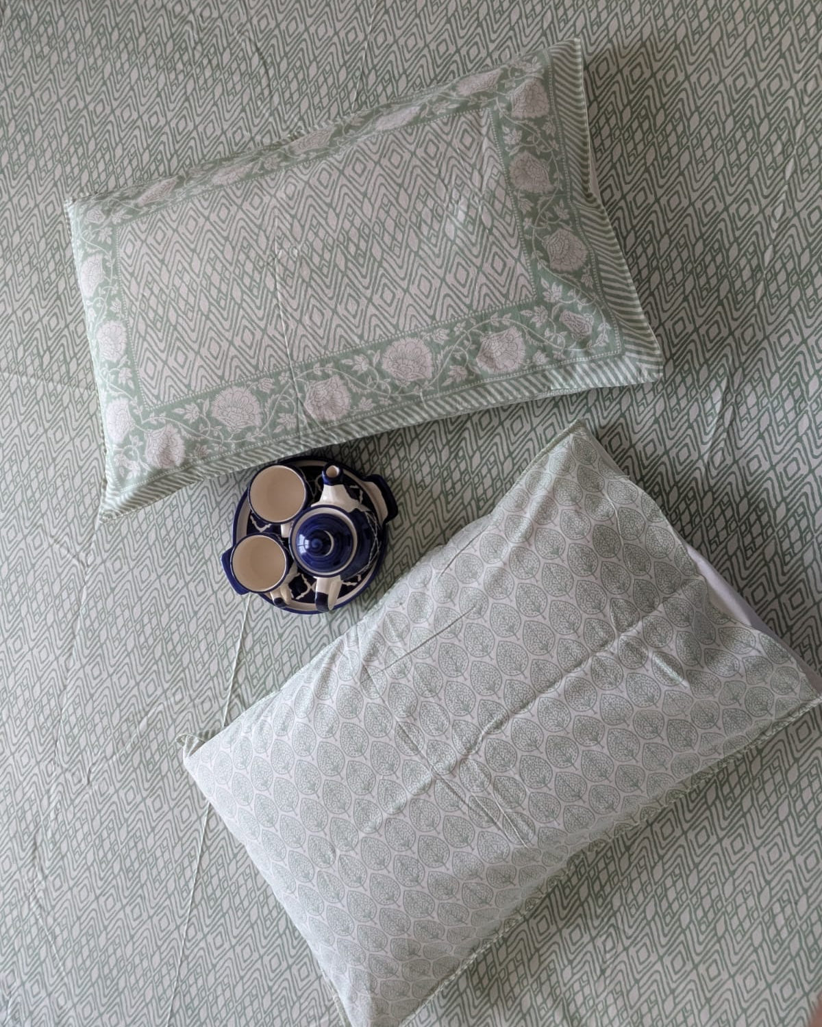 Two patterned pillows on a textured bedsheet with a decorative item in the center.