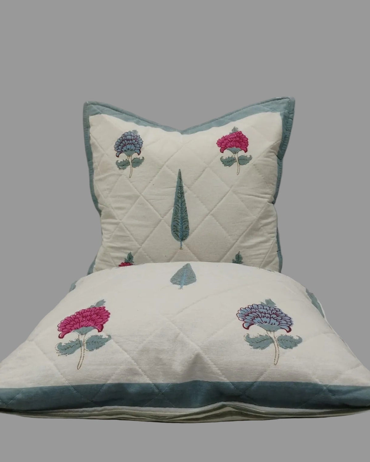 Two Tarangini blue quilted cushion covers stacked to show the floral print and teal trim