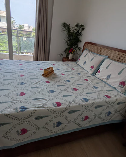 Blue lotus jaal cotton bedsheet with pink and blue floral motifs styled on a cane headboard bed