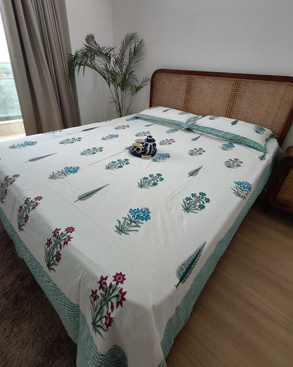 Teal and magenta floral booti cotton bedsheet with a teal-green border on a cane bed