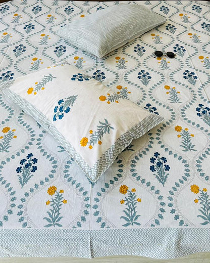 Bed with floral patterned bedspread and pillows against a wooden headboard.