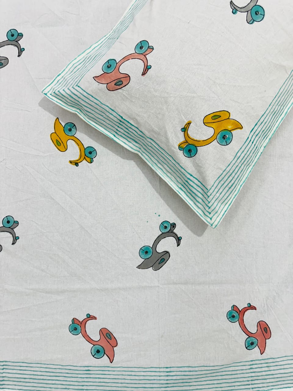 Close-up of white cotton fabric with a colourful hand block scooter print and teal striped border