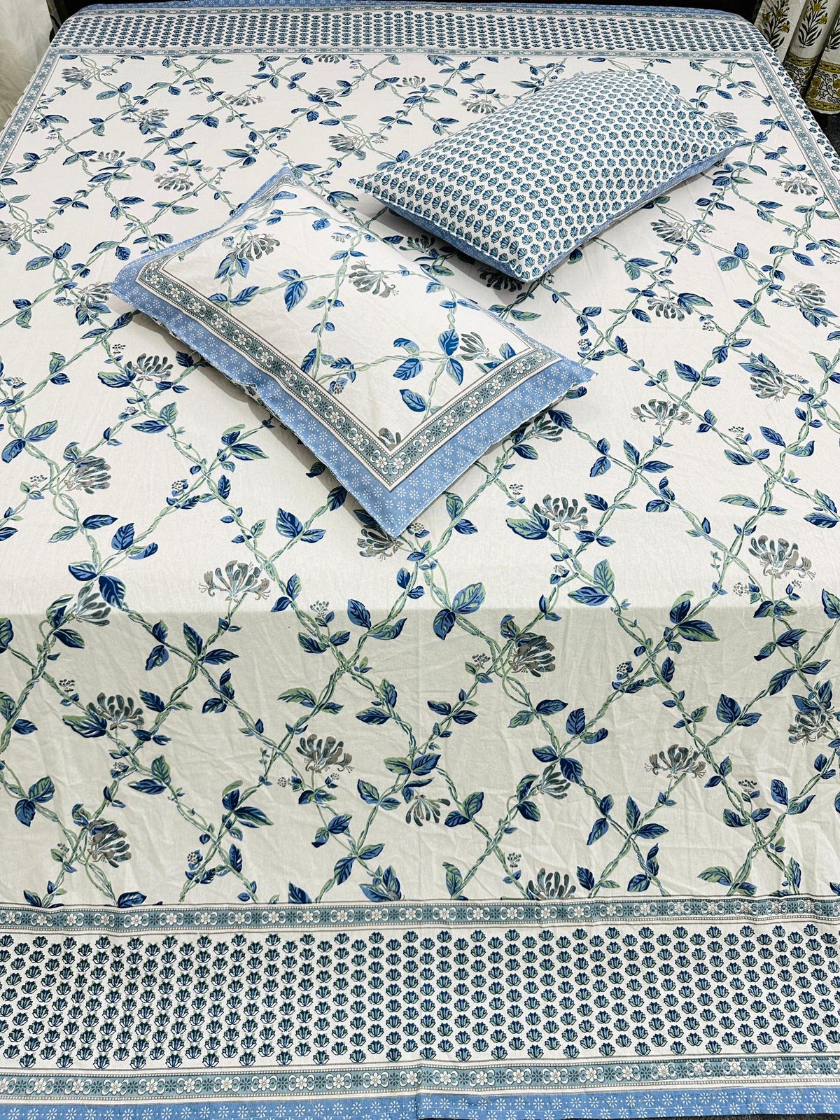 Blue floral cotton bedsheet with two pillow covers and a blue dotted border, overhead view